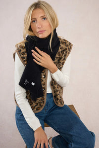 Model sitting on stool, styling black scarf with embroidered white bow