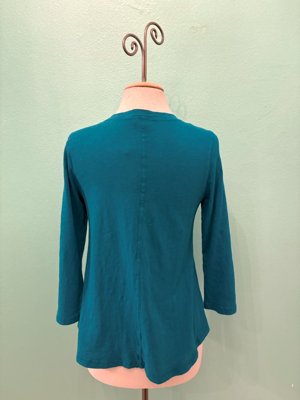 Back view of a teal 3/4 sleeve women's top displayed on a mannequin