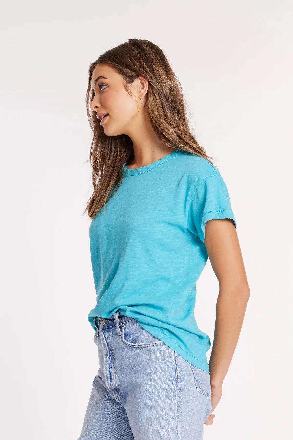 Side profile of woman in a turquoise blue T-shirt and denim jeans