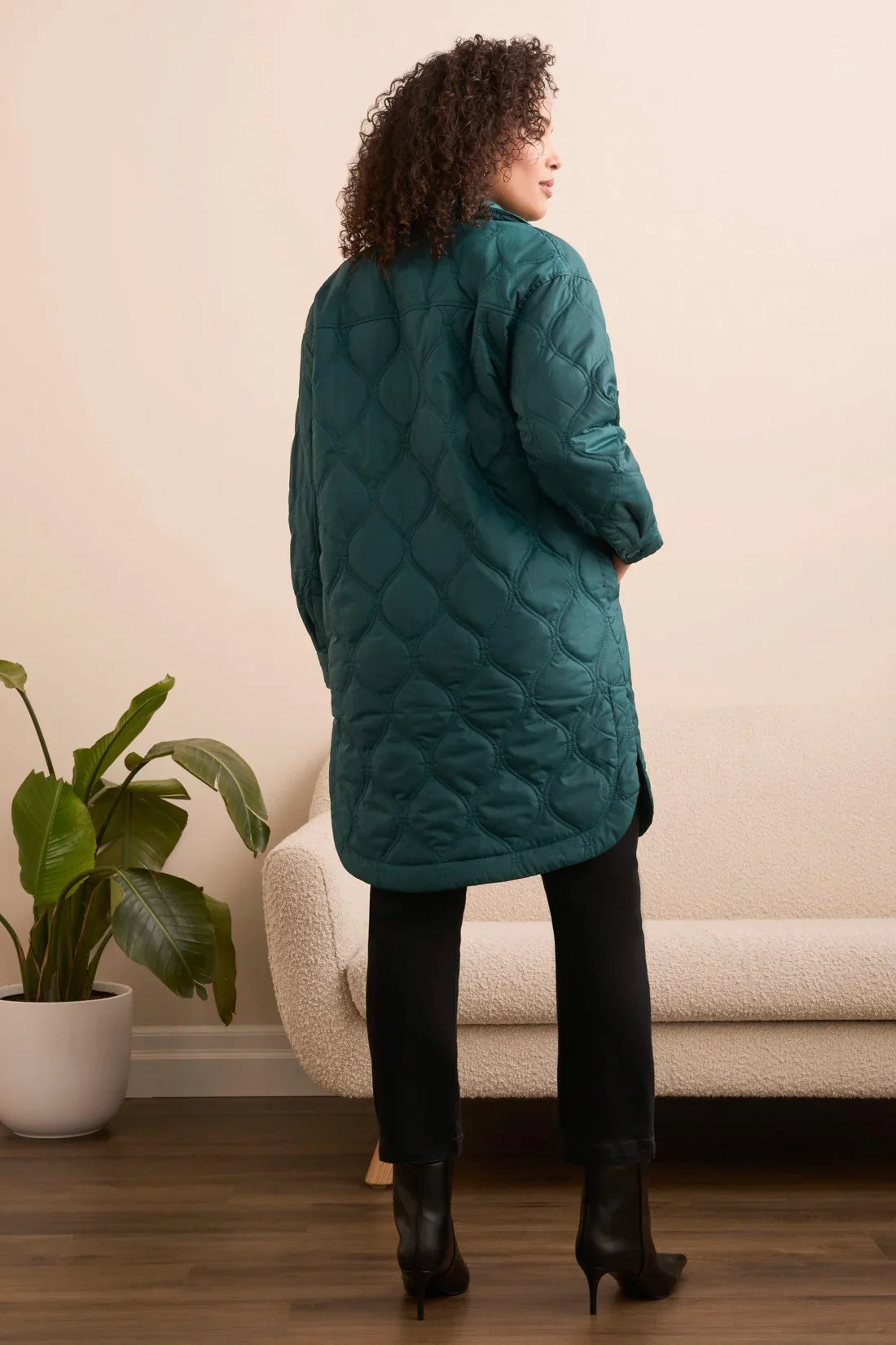 Back view of a woman wearing an evergreen quilted longline jacket, styled with black pants and boots.