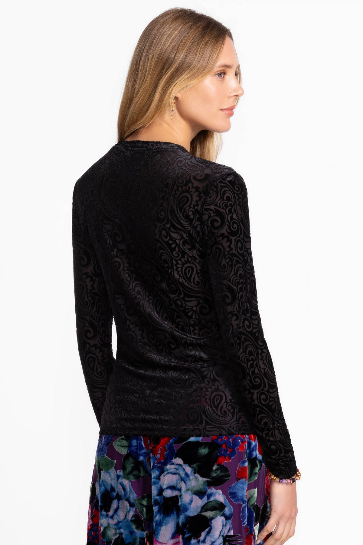 Rear view of a woman in a fitted black velvet paisley long sleeve top paired with floral pants