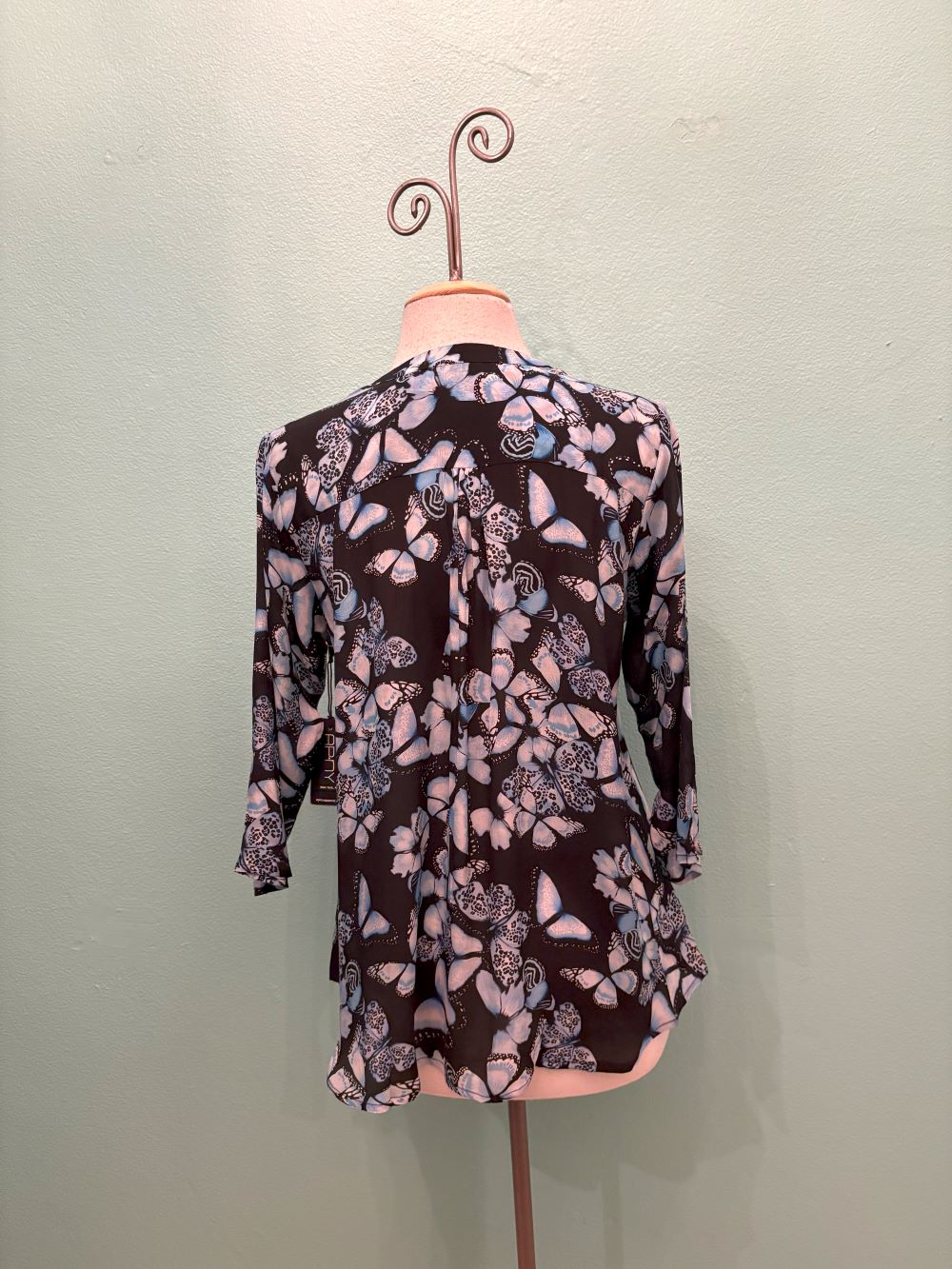 Back view of a flowy black blouse with blue butterfly prints on mannequin