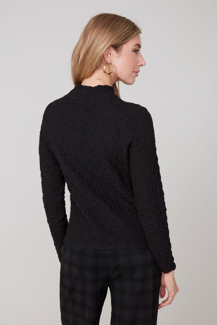 Back view of a woman in a textured black mock neck long sleeve top
