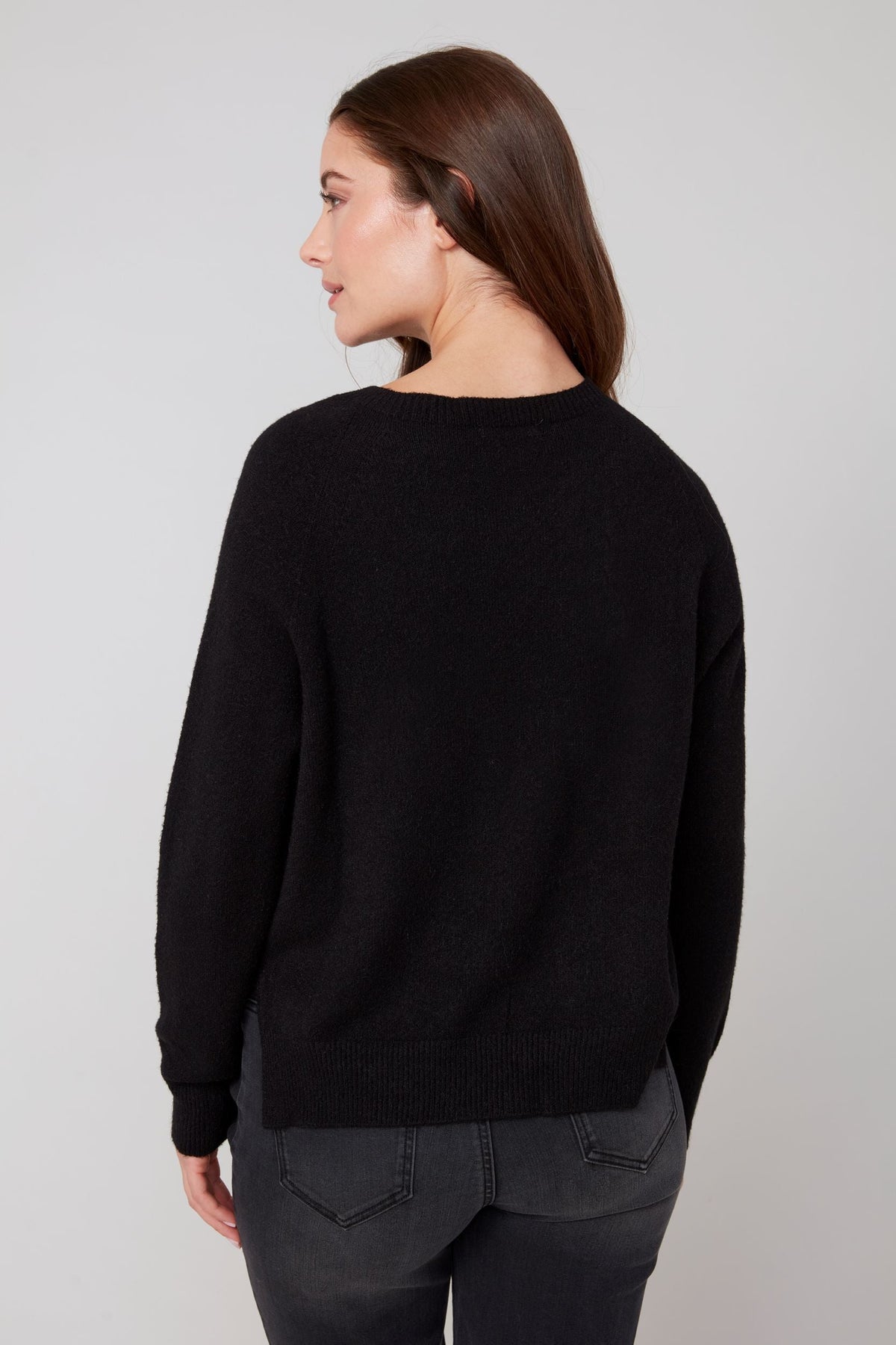 Back view of a woman wearing a classic black crewneck sweater and dark jeans