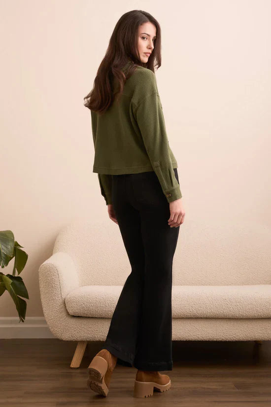 Woman modeling olive green waffle knit button-up shacket and black flared pants, back view