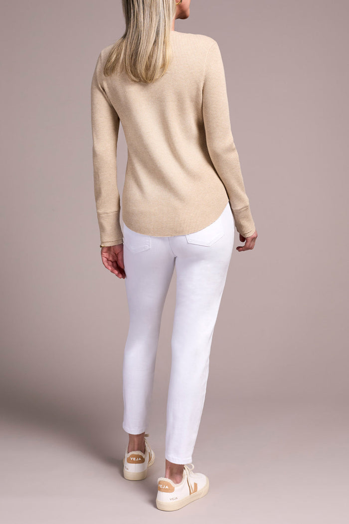 Back view of woman wearing a beige long sleeve Henley top and white jeans