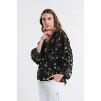 Model posing in a black floral chiffon blouse with loose sleeves and white pants