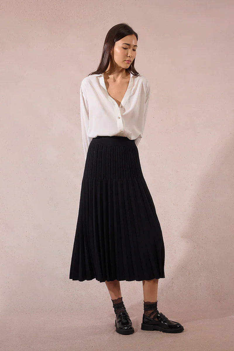 Model looking down in black knit pleated midi skirt and white blouse