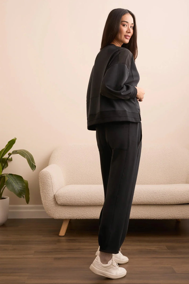 Woman modeling a black lounge set with sweatshirt and joggers, relaxed fit