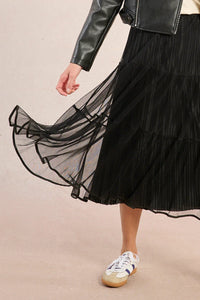 Model twirling in a black mesh tiered midi skirt with leather jacket and sneakers