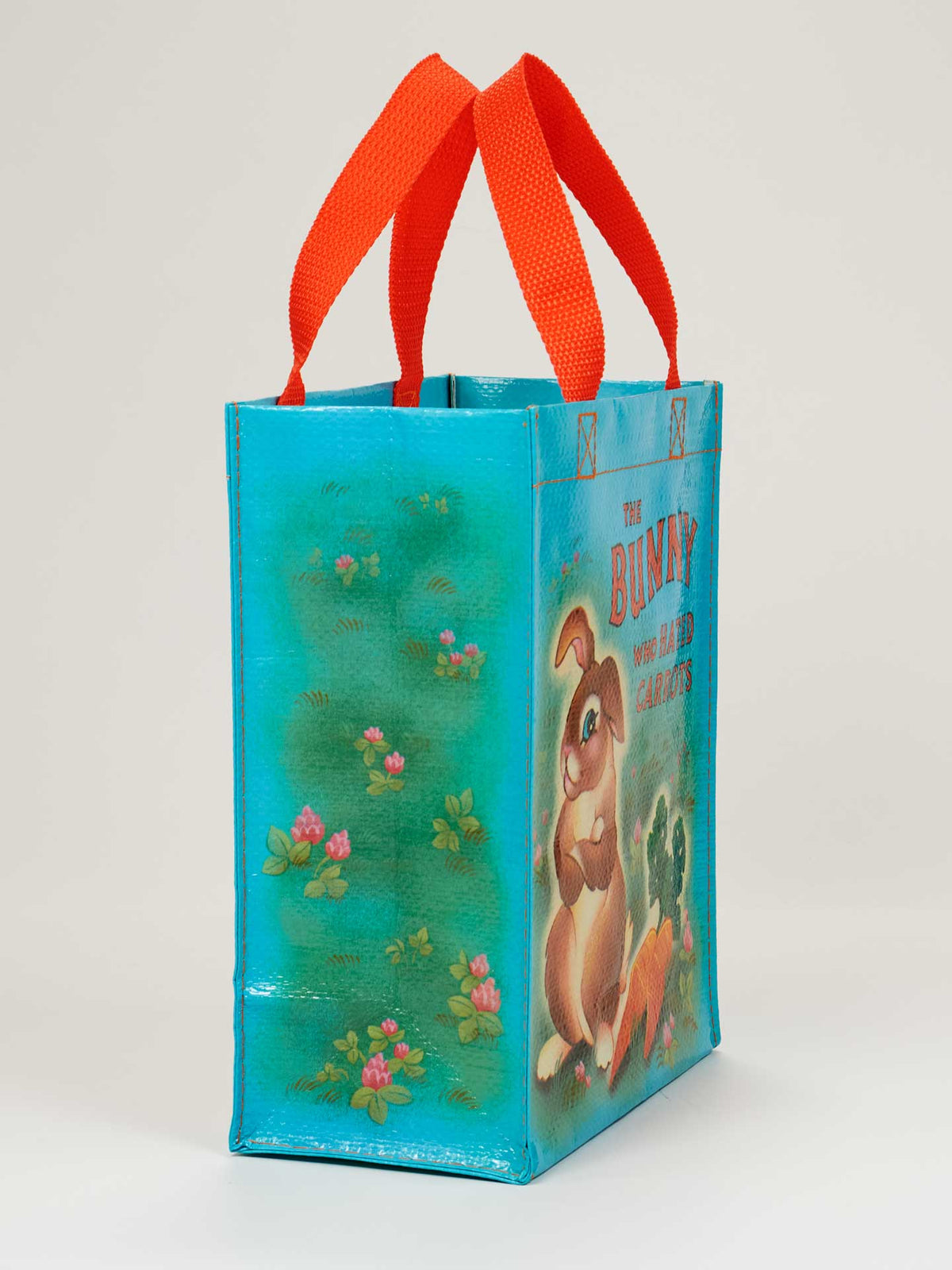 Side view of a blue reusable tote bag with a bunny and carrot illustration, featuring bright orange handles