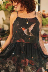 Close-up of the lower half of a black floral maxi dress with ornate border and colorful peonies, roses, and leaves