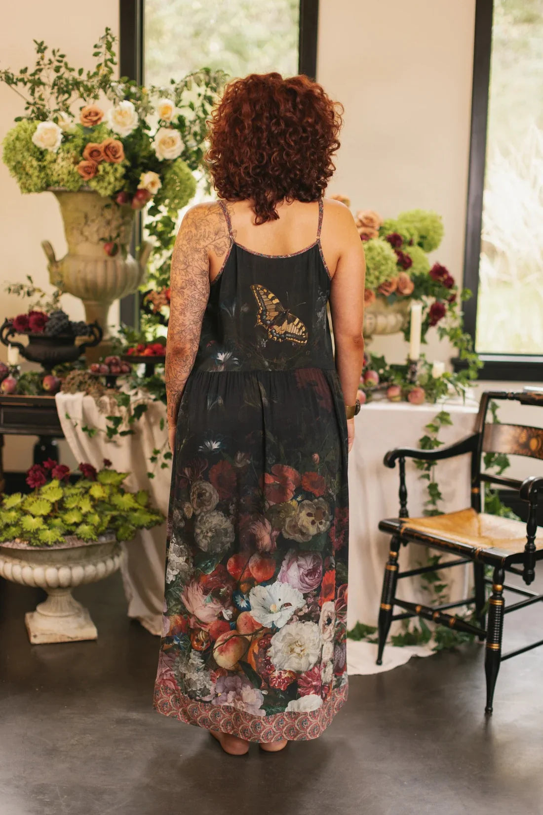 Woman displaying the back of a bohemian floral print dress in a botanical-styled room