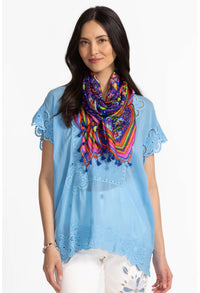 Woman wearing a blue eyelet blouse paired with a vibrant, floral tassel scarf