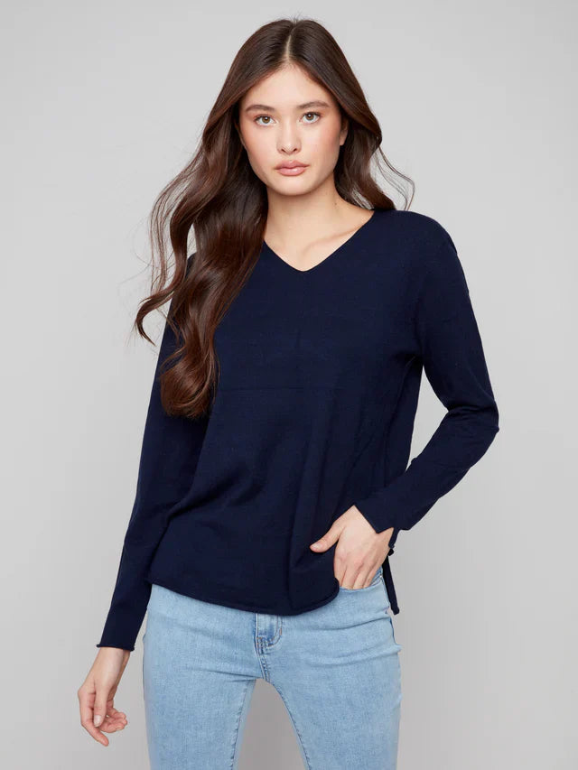 Woman in navy v-neck sweater standing with one hand in her pocket