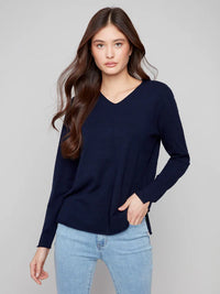 Woman in navy v-neck sweater standing with one hand in her pocket