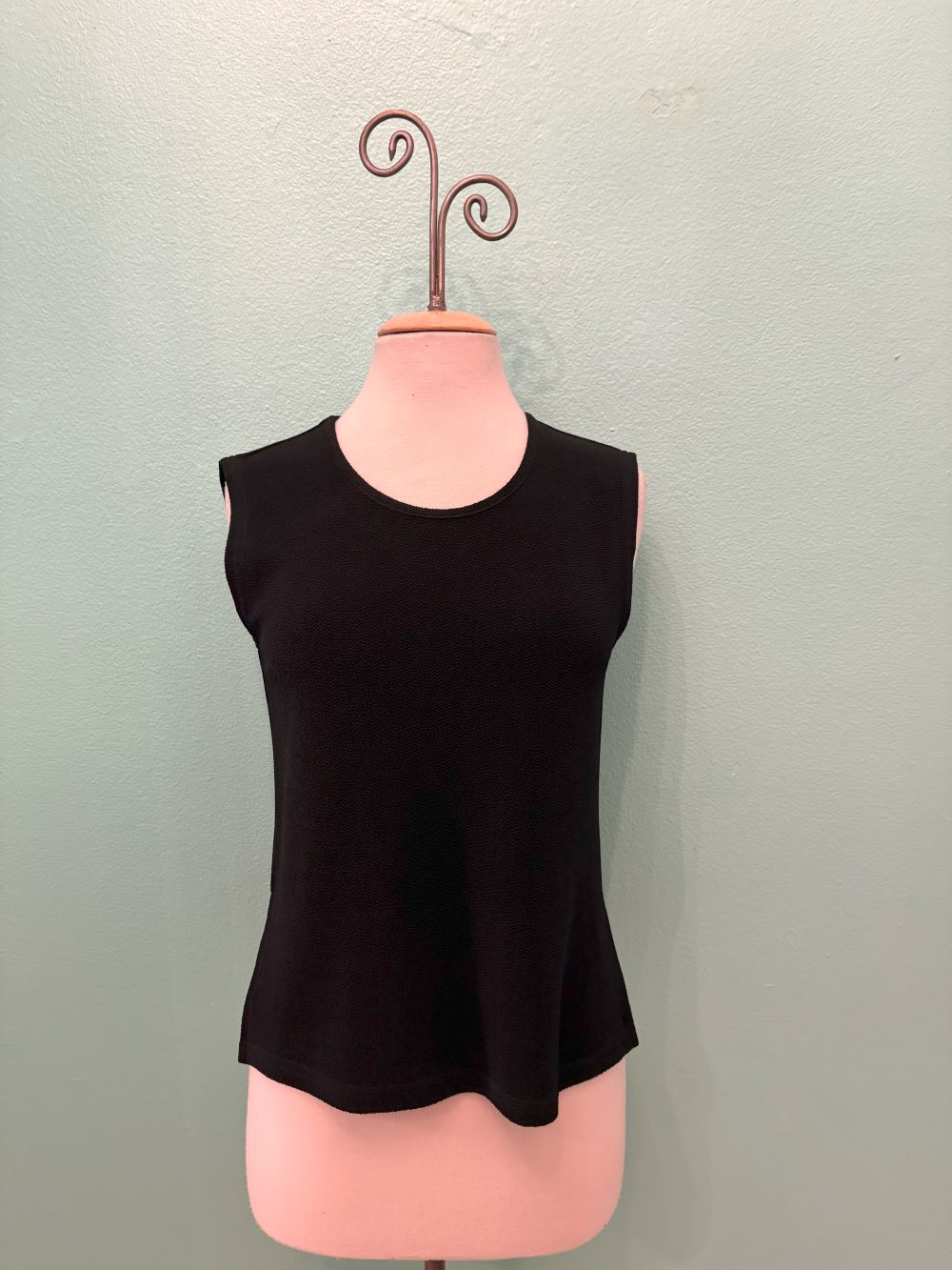 Front view of a classic black sleeveless knit top displayed on a mannequin