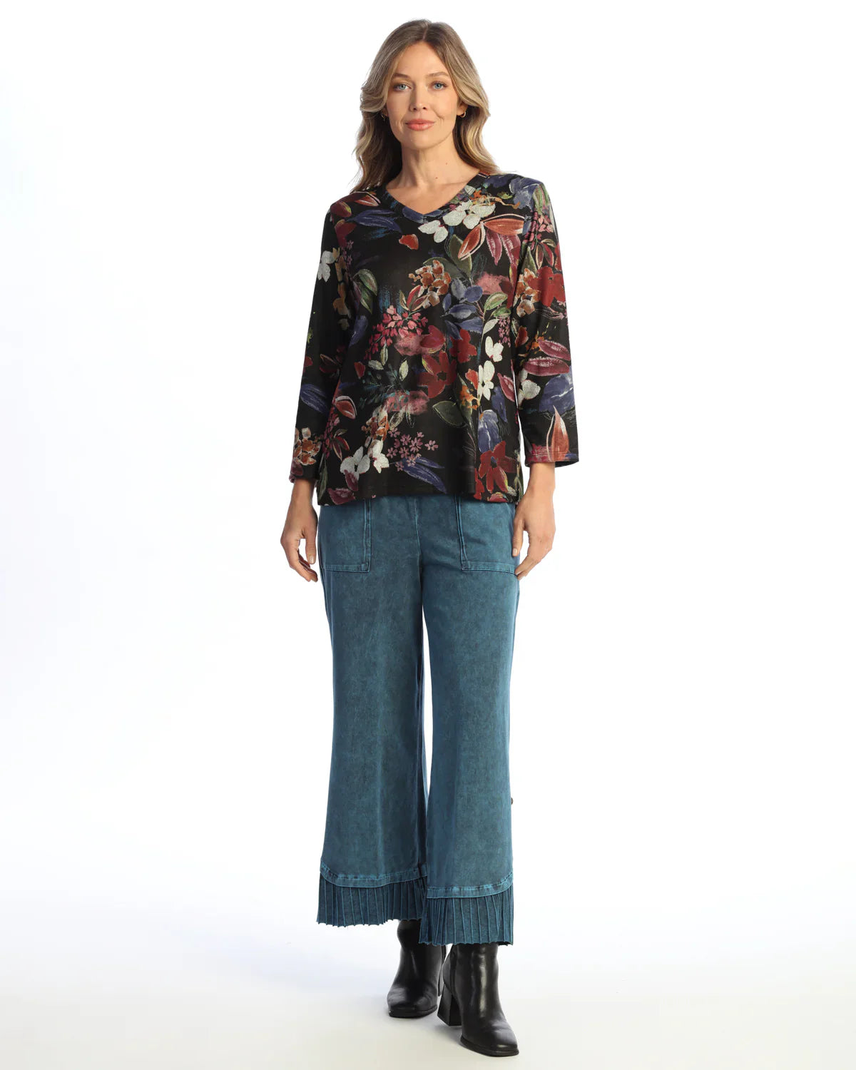 Woman wearing a 3/4 sleeve black top with colorful floral prints and blue denim pants