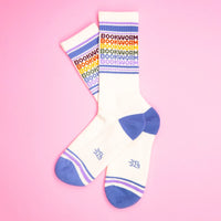 Two Bookworm rainbow gym socks crossed on a pink background, showing colorful text and stripes