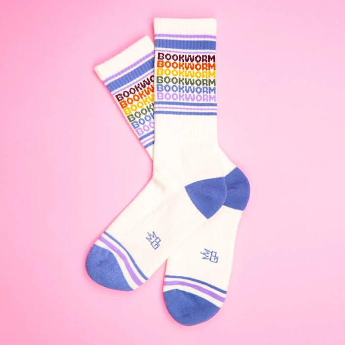 Two Bookworm rainbow gym socks crossed on a pink background, showing colorful text and stripes