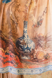 Close-up of scarf showing blue vase, butterflies, and floral artwork in soft earth tones