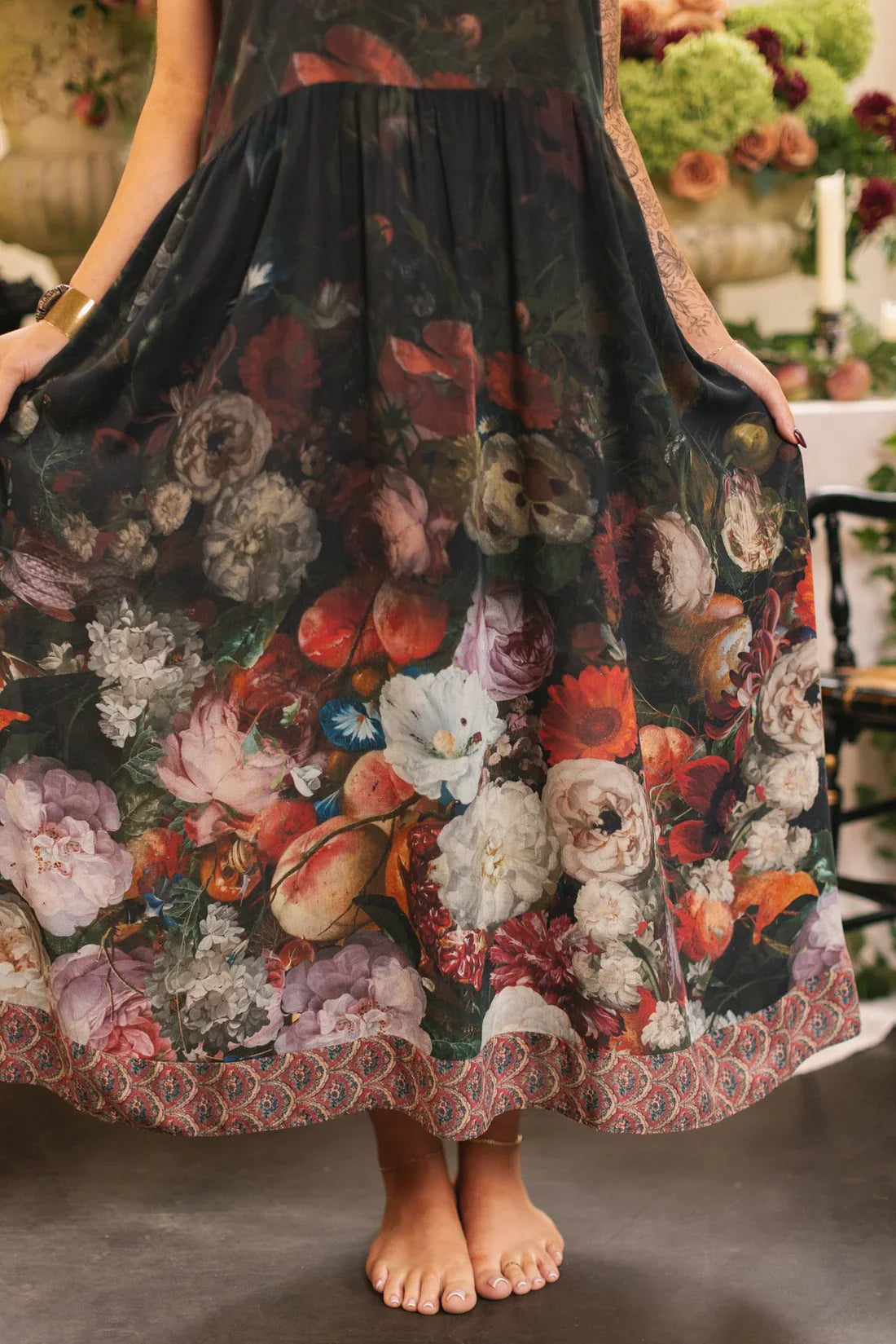 Close-up of the lower half of a black floral maxi dress with ornate border and colorful peonies, roses, and leaves