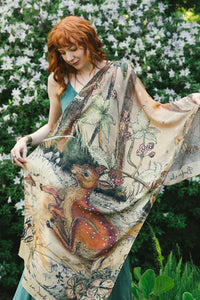Woman draped in illustrated fawn and brambles scarf amid blooming garden