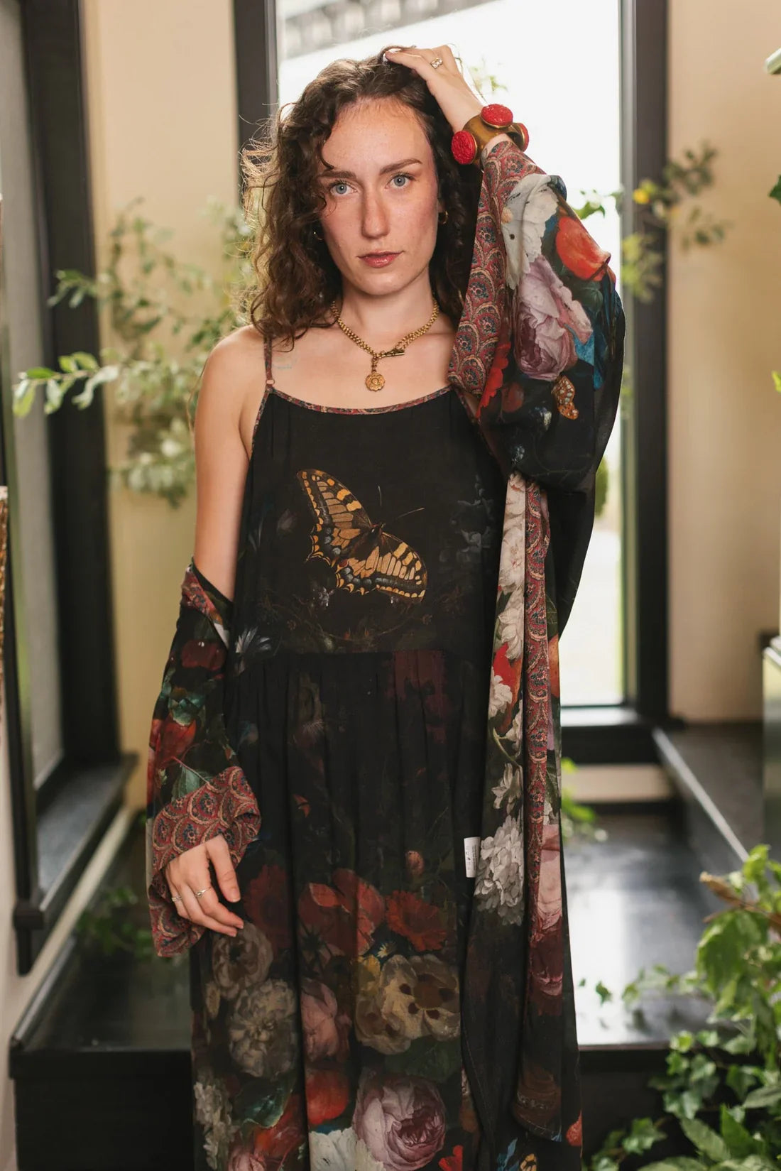 Woman modeling a sleeveless black dress adorned with vibrant flowers and a large butterfly design