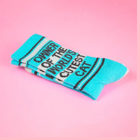 Folded blue cat owner socks with bold black lettering on pink surface