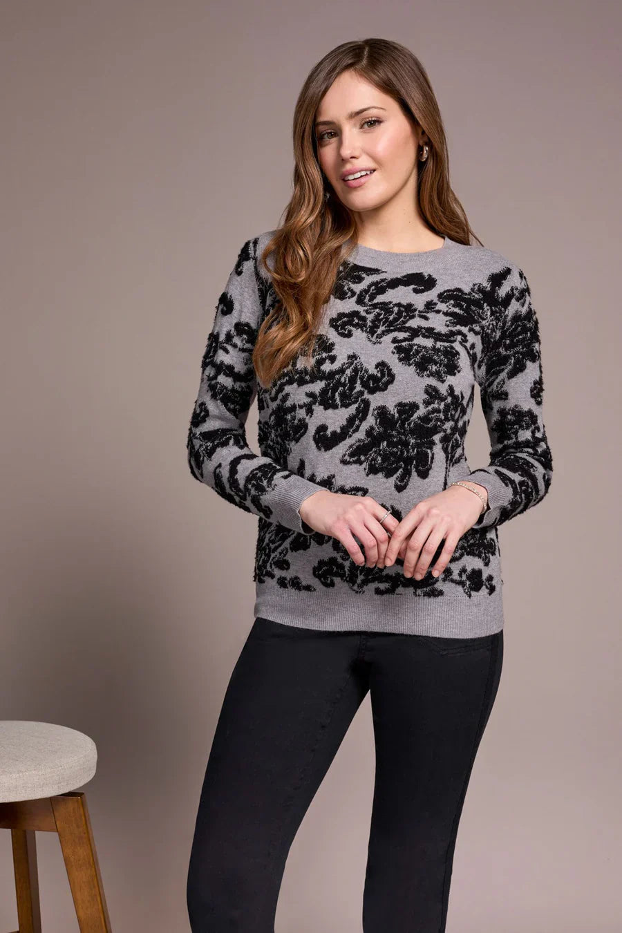 Front view of a woman in a grey sweater with bold black floral jacquard pattern and black pants