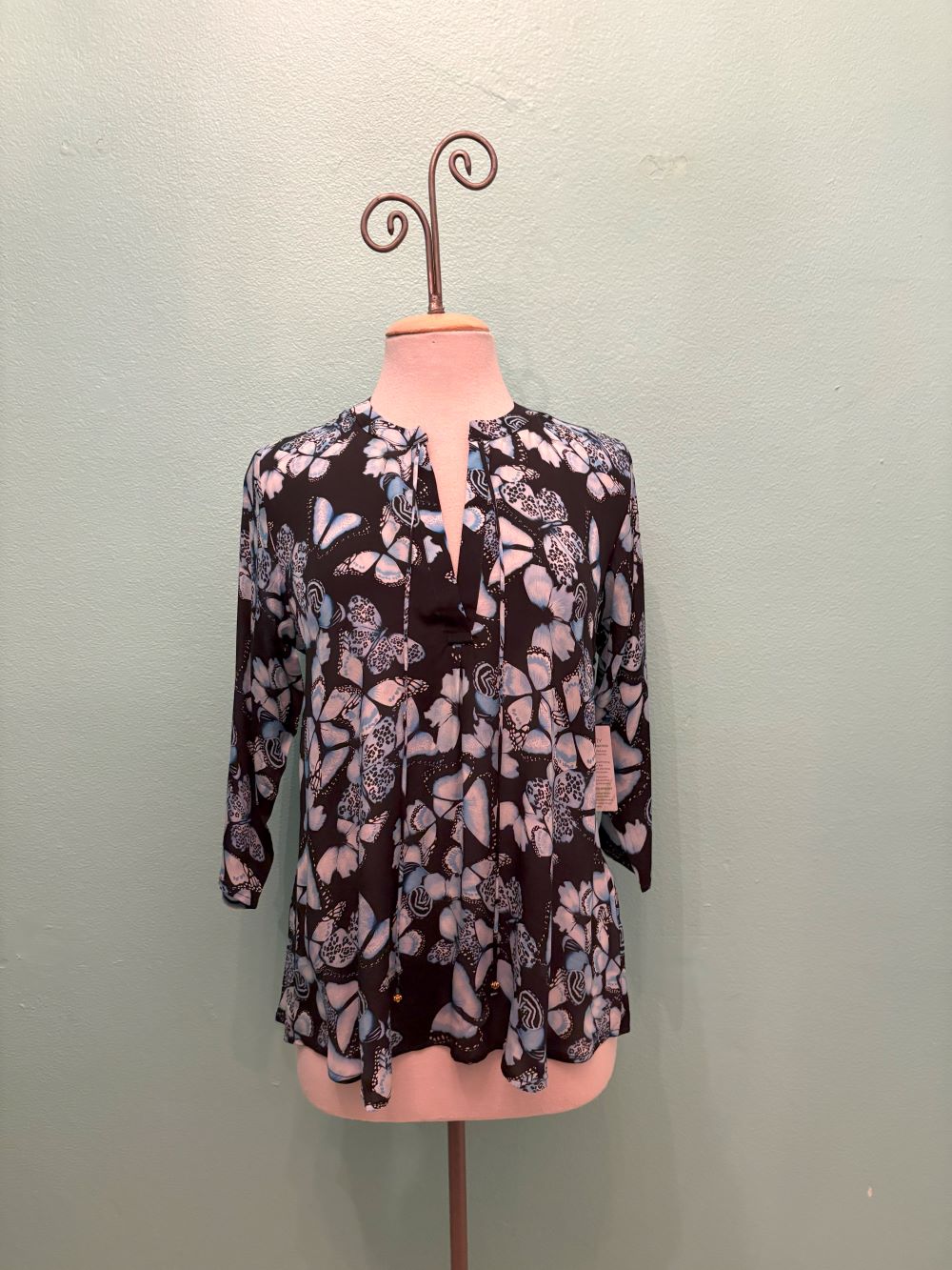 Front view of a black blouse with blue butterfly design on mannequin