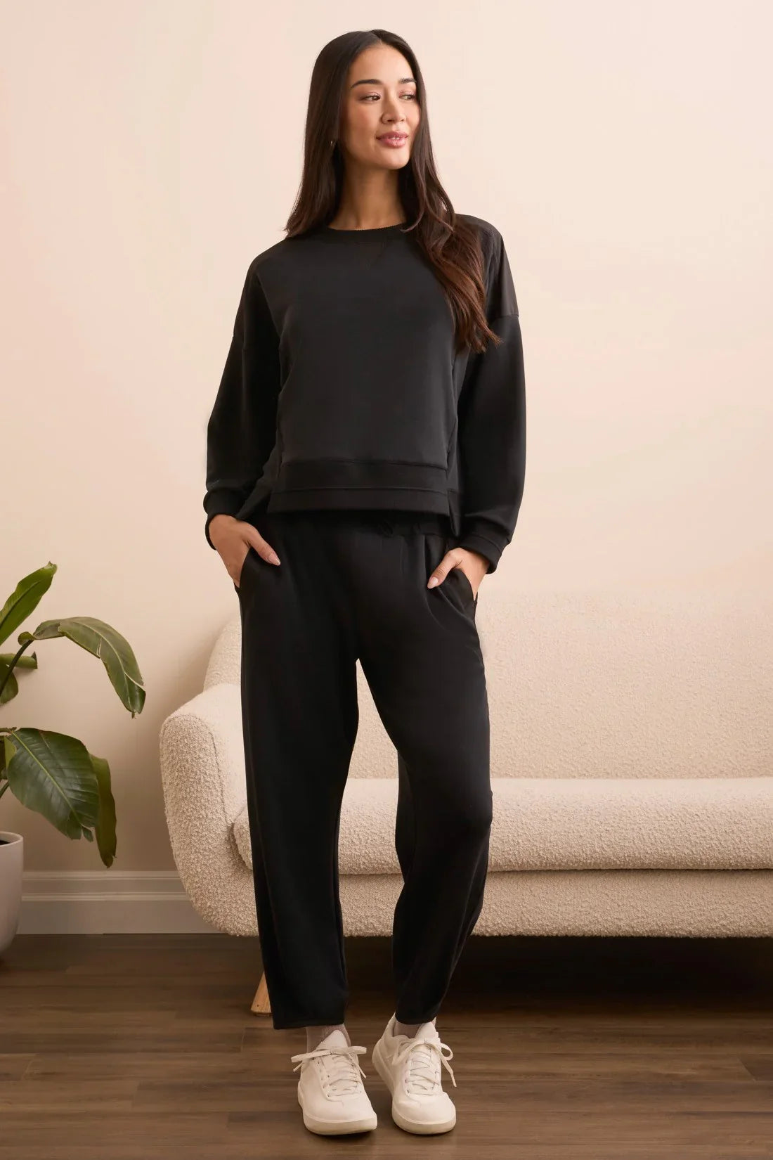 Woman standing in black lounge set with hands in pockets, front view