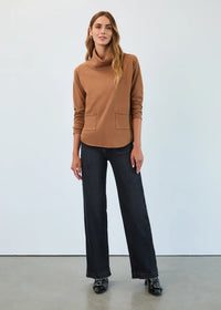 Woman wearing a camel funnel neck pullover with two front pockets and dark jeans
