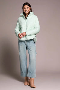 Front view of a smiling woman in a mint quilted puffer jacket with relaxed denim and nude boots