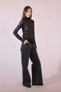 Model in wide-leg pants and black sheer lace turtleneck posing stylishly