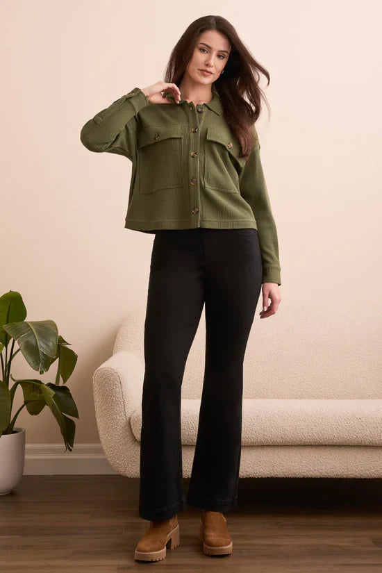 Full body shot of woman in olive green waffle button-up shacket with black pants and brown platform shoes