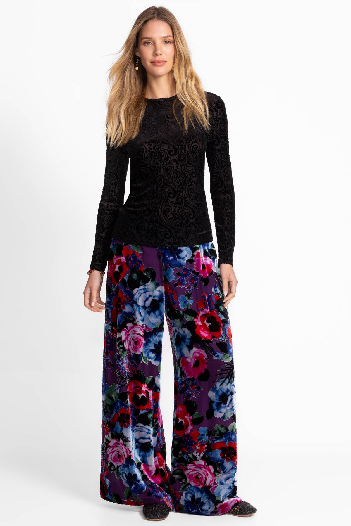 Full-length view of a woman dressed in a black velvet paisley long sleeve top and colorful floral pants