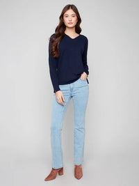 Full body shot of woman in navy v-neck sweater and light blue jeans with brown boots