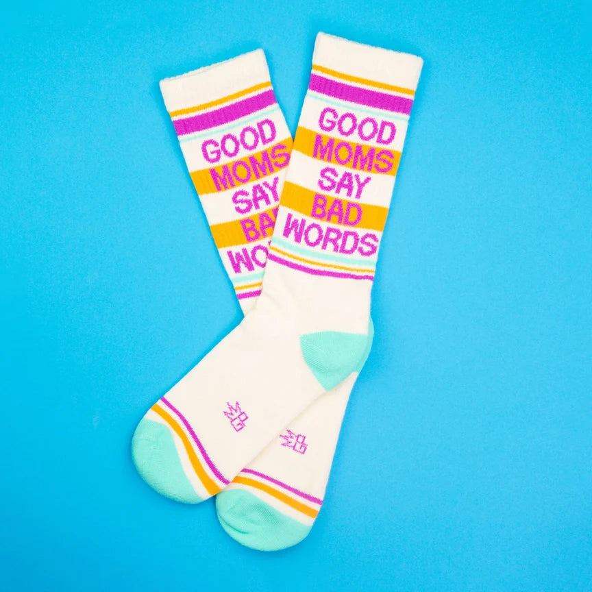 Two cream socks with 'Good Moms Say Bad Words' text on a vibrant blue surface