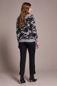 Back view of a woman wearing a grey sweater with black floral jacquard design and black pants