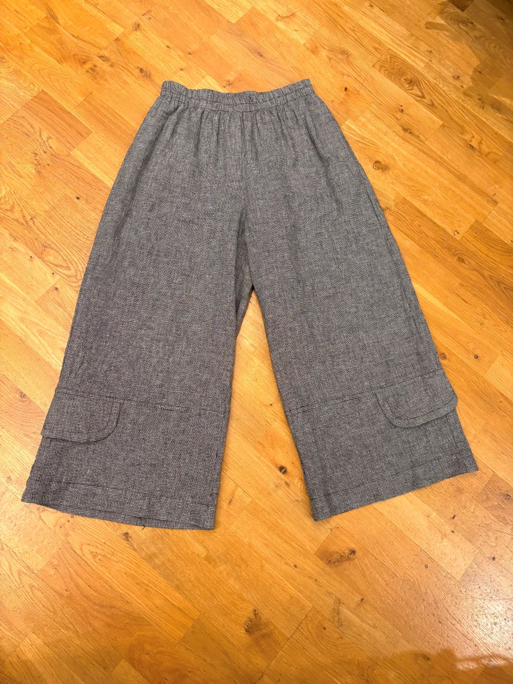 Heather grey wide leg linen pants with flap pockets laid flat on wooden floor