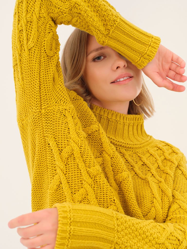 Woman wearing a yellow cable knit turtleneck sweater, closeup showing texture and style