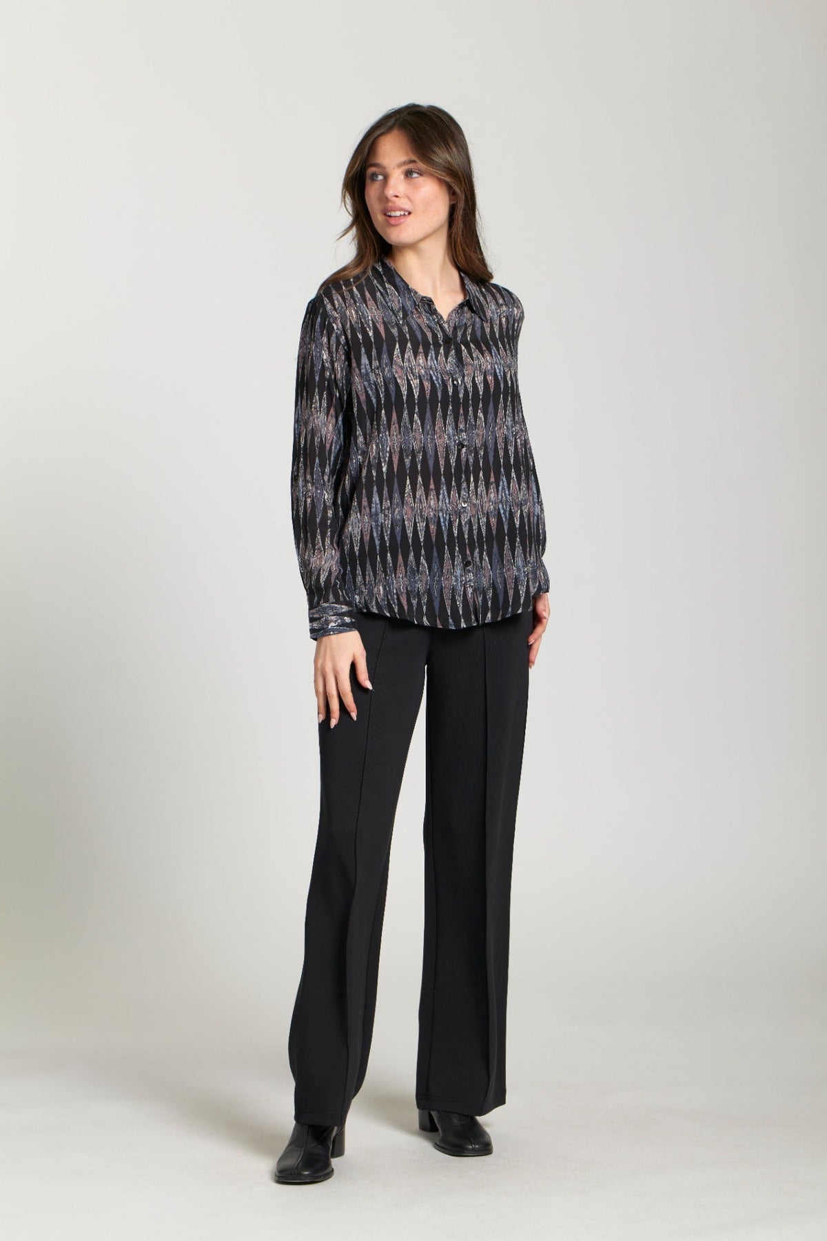 Woman modeling a relaxed fit blouse featuring a black and metallic diamond print with black dress pants