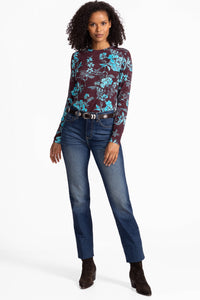 Full body shot of a woman modeling a teal floral print maroon long sleeve shirt with jeans and boots