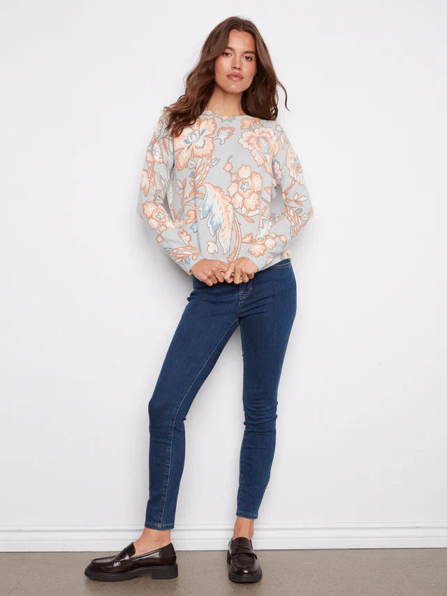Woman in pastel floral sweater paired with skinny blue jeans and black loafers
