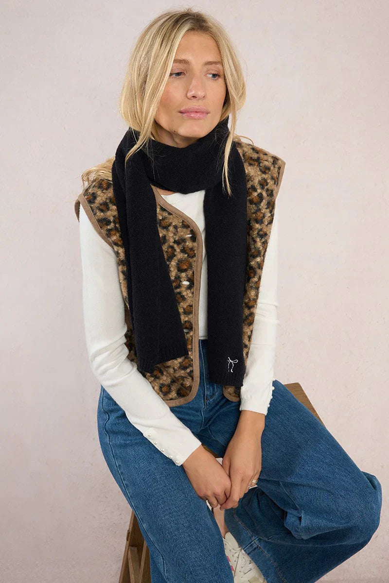 Model sitting, dressed in leopard vest and blue jeans with black scarf