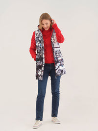 Woman wearing coral cable knit sweater, jeans, and printed vest, smiling