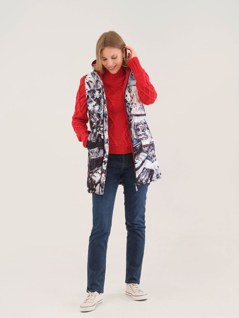 Woman wearing coral cable knit sweater, jeans, and printed vest, smiling