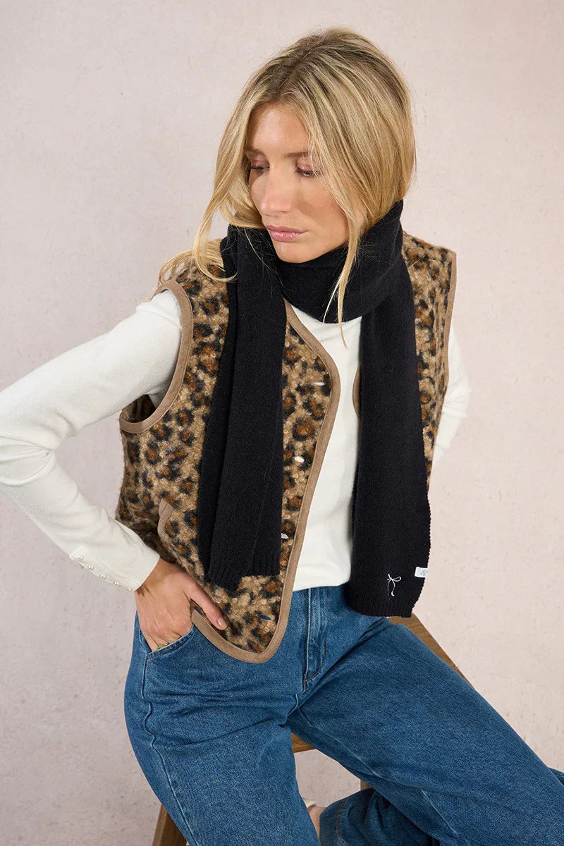 Model sitting on stool, styling black scarf with embroidered white bow