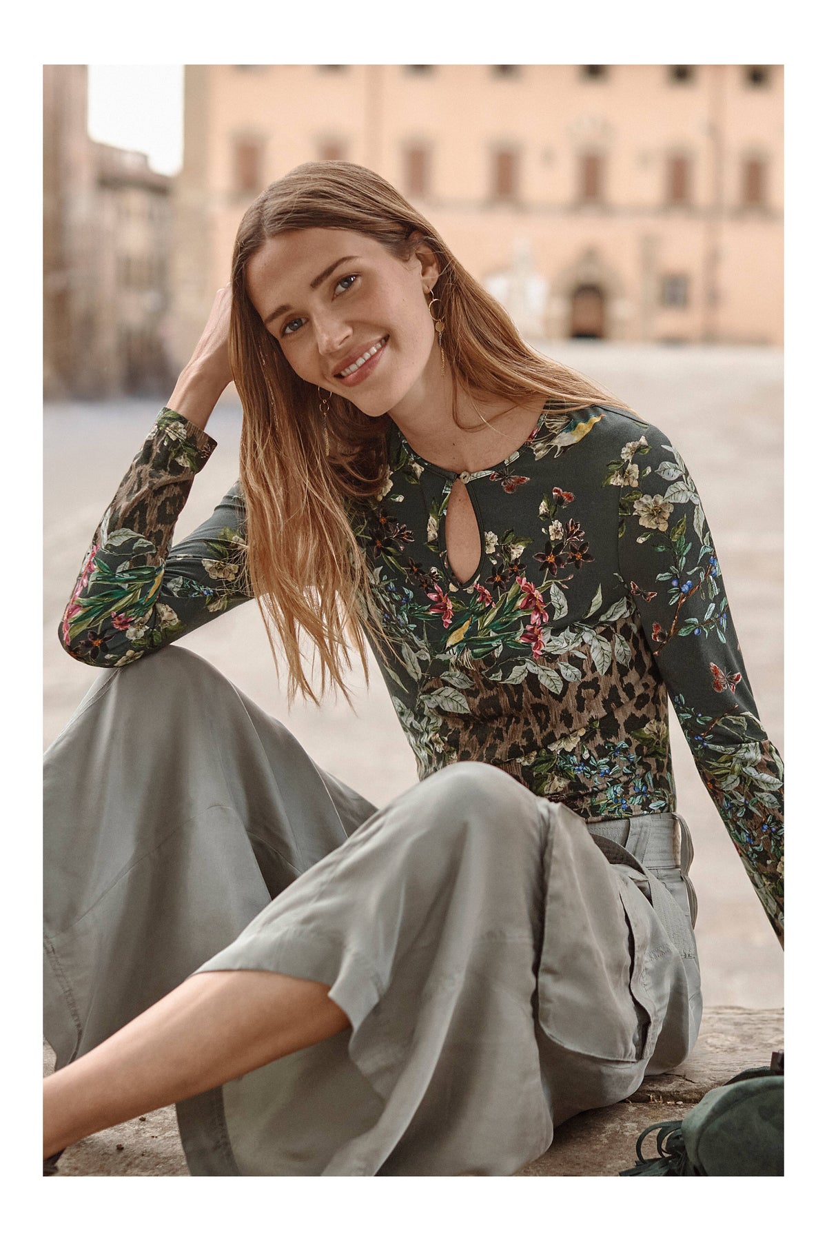Smiling woman in floral and leopard print keyhole top, sitting outdoors